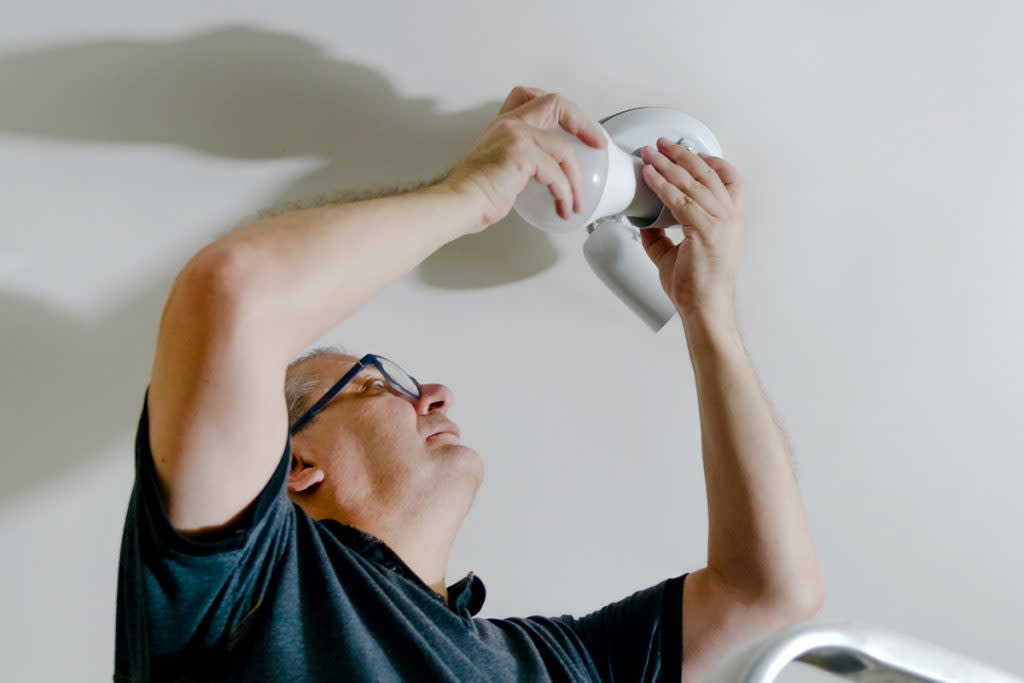 A man replaces a light bulb on a light fixture attached to his ceiling. 