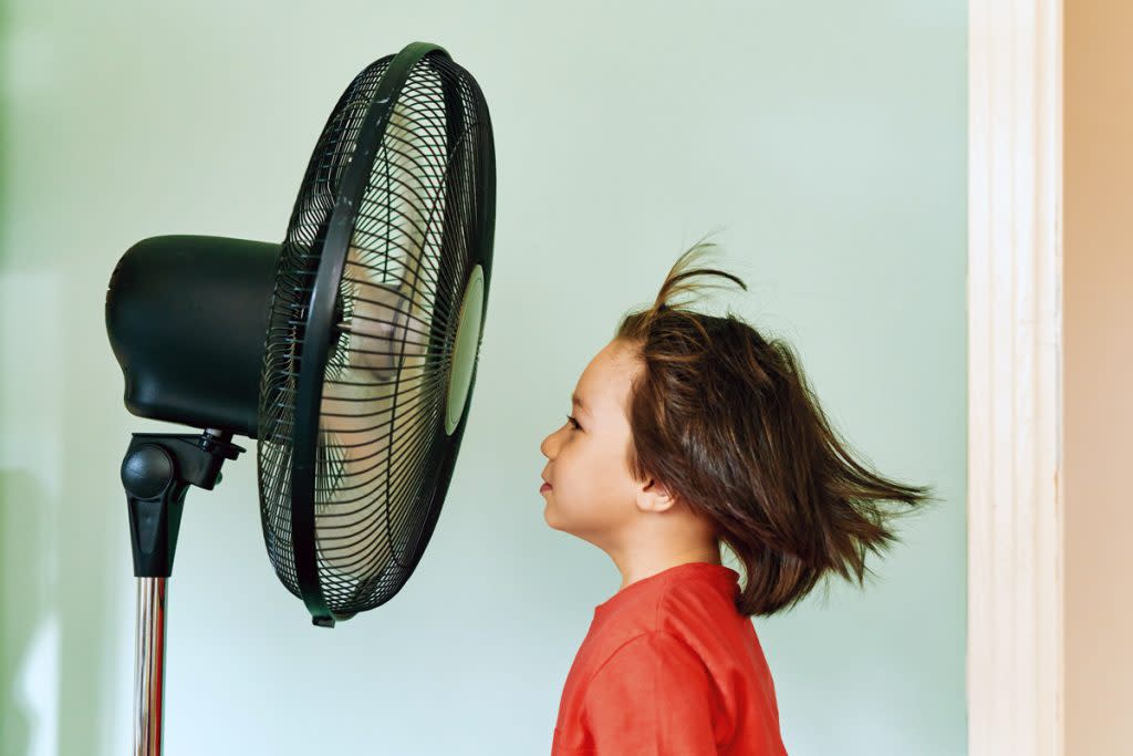 A boy stands in front of a fan that blows his hair up in the air. 