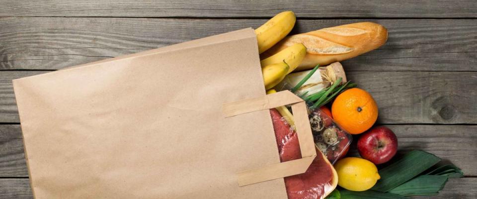 Different food in paper bag on wooden background, close up.
