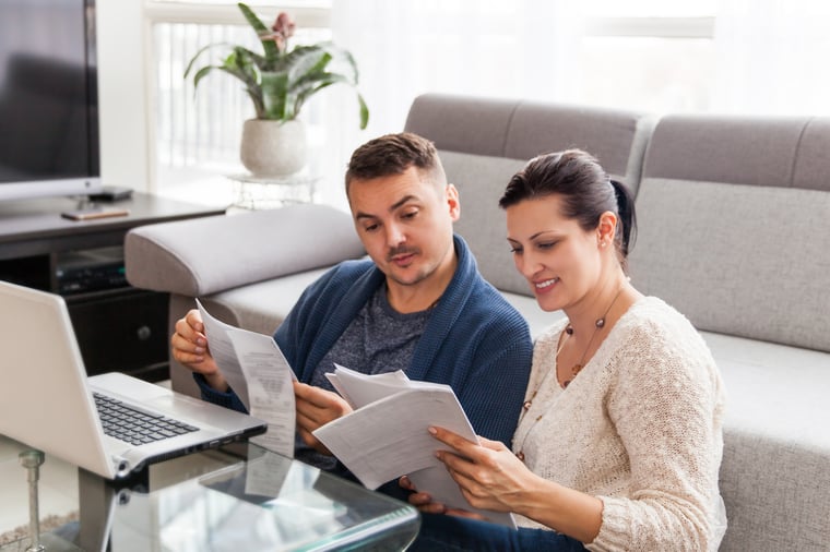 A couple sitting on the floor of their living room organizing paperwork.